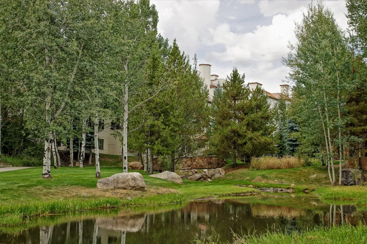 This peaceful scene showcases a pond bordered by rocks, trees, and a view of the building in the background. It suggests moments of quiet reflection, nature observation, or simply enjoying the outdoors—key elements of a relaxing, resort-style stay.