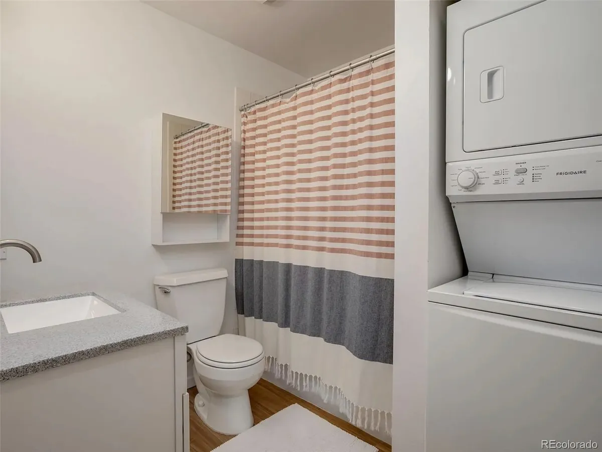 A functional laundry area featuring a stackable washer and dryer, a vanity sink, and a mirror. The area is tidy, efficient, and clearly integrated for guest convenience.