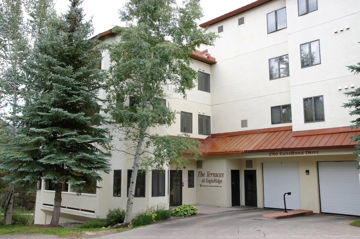 This image displays the building's exterior facade with inviting landscaping, an entrance sign, and groups of people socializing on the terrace. The atmosphere is lively yet serene, suggesting a welcoming hub where guests gather and enjoy moments before heading out to nearby attractions.