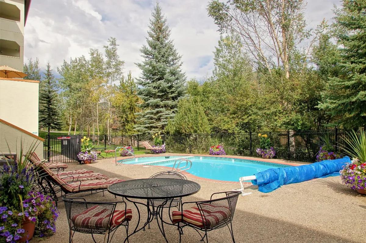 A vibrant outdoor pool area surrounded by lush greenery and colorful flowers. Lounge chairs and outdoor seating invite guests to relax, swim, sunbathe, or gather for meals. The poolside setting offers an ideal spot for après-ski relaxation or soaking up the summer sun.