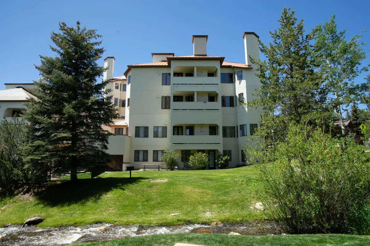 This image captures a three-story building set against a lush green lawn, with a flowing stream meandering through the landscape. The outdoor setting is tranquil and inviting, perfect for relaxing, picnicking, or enjoying nature walks. The presence of trees and open grassy spaces highlights the natural beauty right outside the resort.