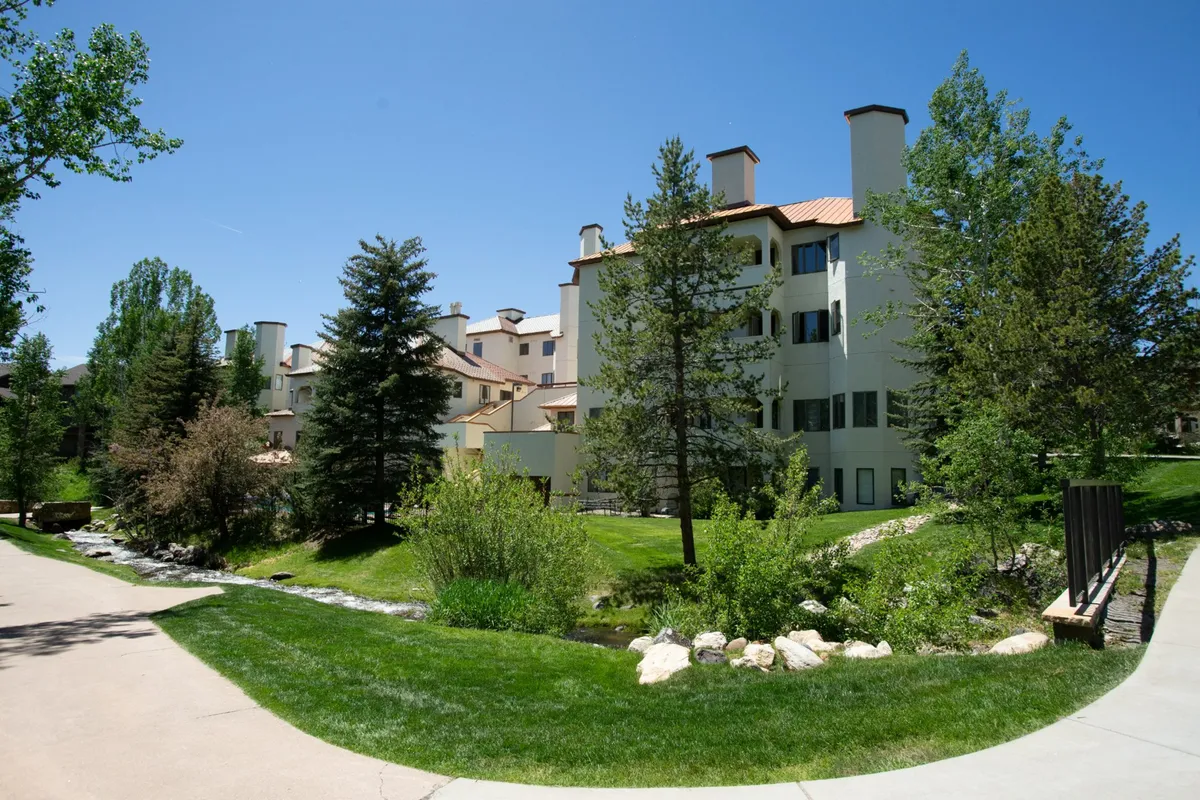 This exterior photo features landscaped gardens, a pathway, and the building nestled among greenery. The tranquil setting hints at opportunities for outdoor relaxation and recreation, promoting the idea of leisurely strolls and gatherings—hallmarks of resort living.
