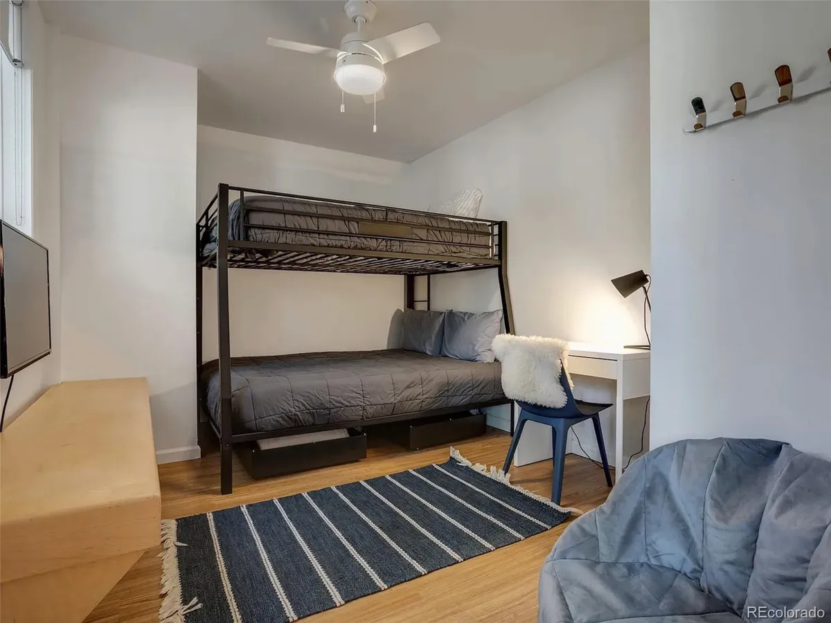 The image shows a room with a stylish Twin-over-Queen bunk bed, a blue chair perfect for reading, a wooden bench, and a striped rug. The space feels inviting and practical, accommodating both rest and relaxation.