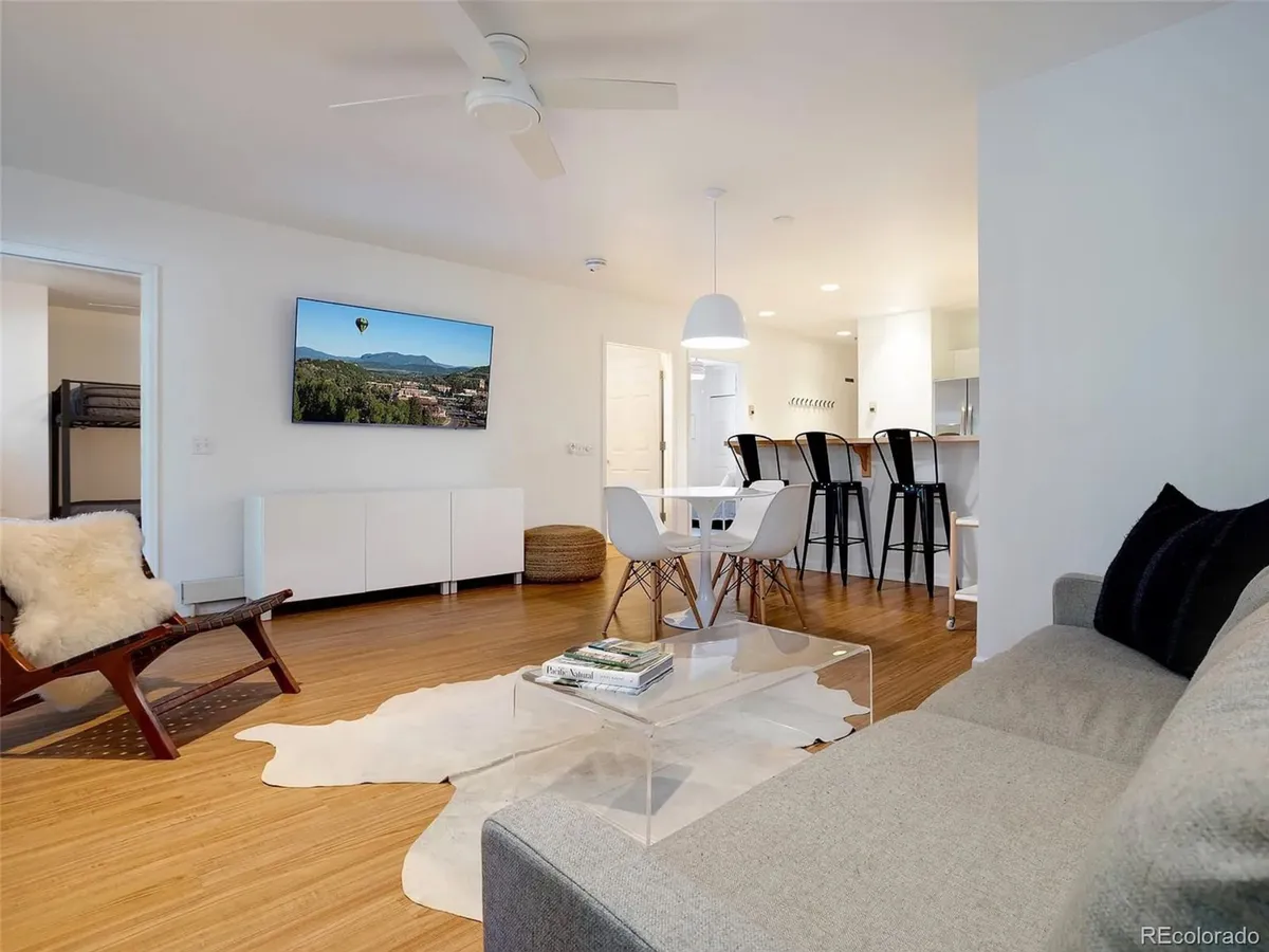 A wide-angle view of the open living area capturing a contemporary sofa, coffee table, large TV, and a dining table in the background. The seamless flow between the living and dining spaces encourages group gatherings and shared moments.
