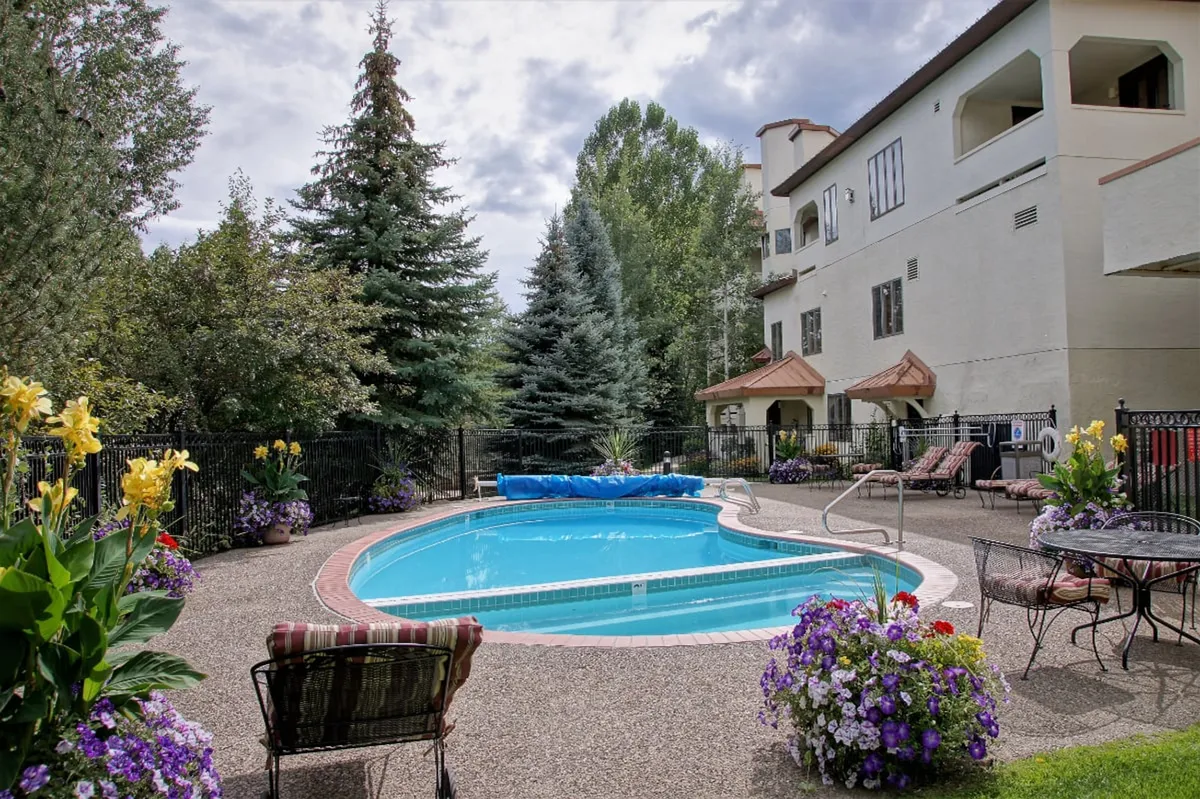 This exterior image highlights a sparkling heated swimming pool with inviting lounge chairs and vibrant flower beds. The pool area is set against the building’s facade, signaling leisure and relaxation throughout the seasons. The combination of water, greenery, and comfortable seating supports both active and restful outdoor experiences.