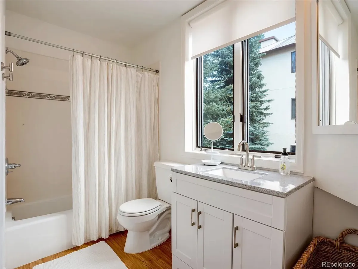 A bright, spa-inspired bathroom featuring a sleek shower area, modern vanity with sink, and a window that lets in soothing natural light. The refined finishes and refreshing atmosphere invite relaxation after a day outdoors.