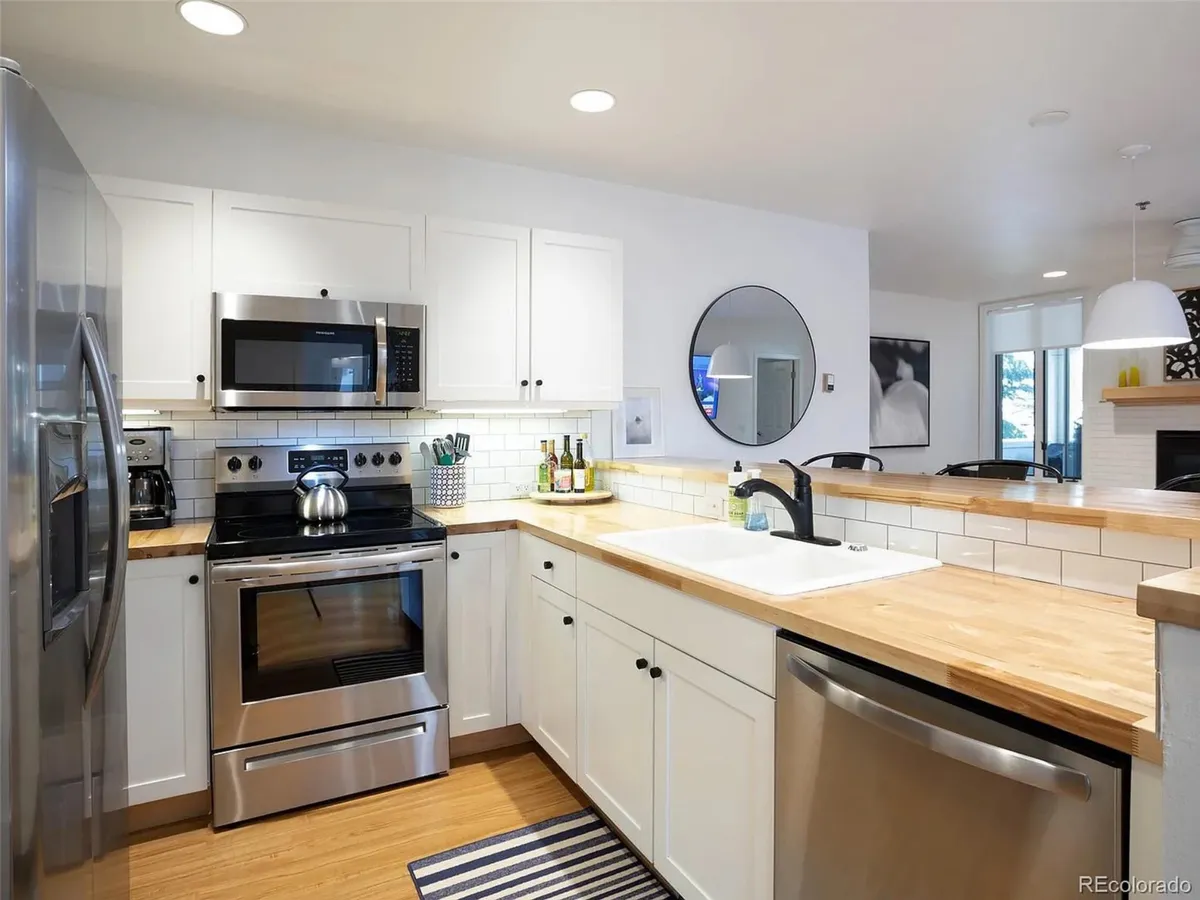 A modern kitchen with stainless steel appliances, wooden countertops, white cabinetry, a decorative mirror, and a functional layout. The space is ready for cooking, entertaining, and socializing around the bar.